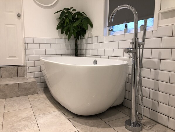 A modern bathroom with a freestanding bathtub, white tiled walls, and a potted plant.