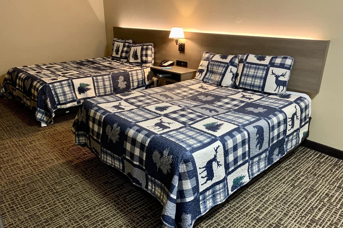 Habitación de hotel con dos camas, cada una con colcha de cuadros estampada con motivos de animales, una mesita de noche con lámpara y teléfono.
