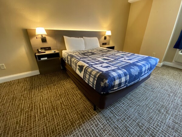 A hotel room with a large bed, two bedside tables, a nightstand, a lamp, and a carpeted floor.