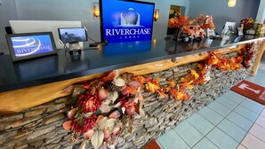 Un mostrador de recepción con el letrero de Riverchase Lodge, un monitor de computadora, una tableta y adornos con temática otoñal.