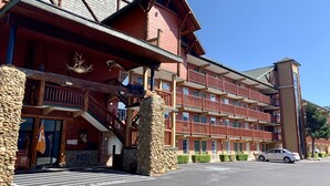 Un hotel de varios pisos con fachada de piedra, balcones y una zona de estacionamiento.