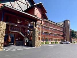 A multi-story hotel with a stone facade, balconies, and a parking area.