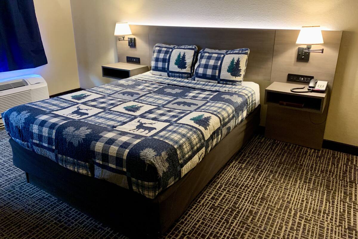 Una habitación de hotel con una cama grande, dos mesitas de noche, una lámpara y un teléfono en la mesita.