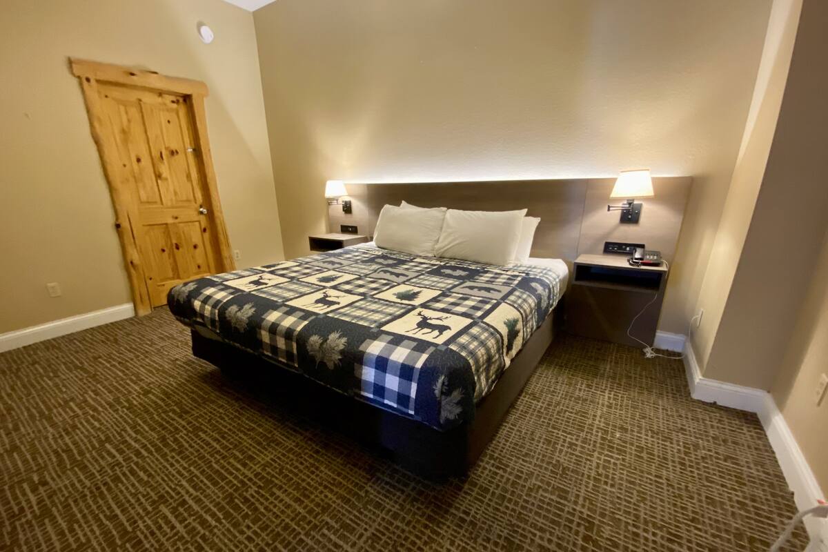 Una habitación de hotel con una cama grande, una puerta de madera y dos mesitas de noche con lámparas.