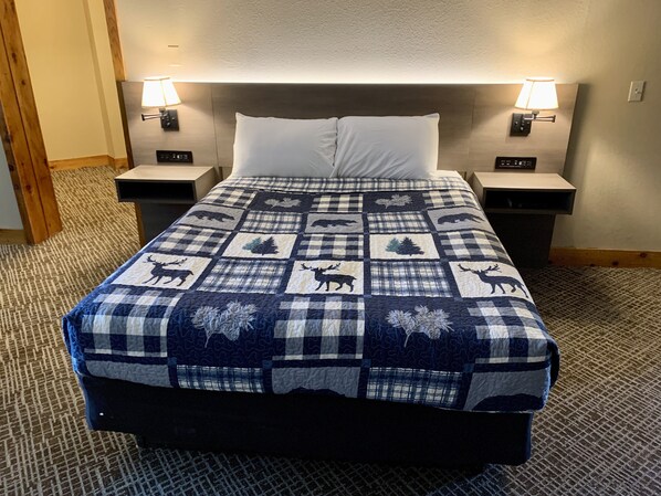 Una habitación de hotel con una cama grande, dos mesitas de noche y dos lámparas fijadas a la pared.