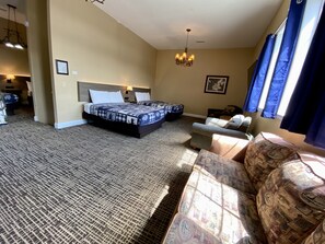 A hotel room with a large bed, a sofa, a desk, and a chandelier.