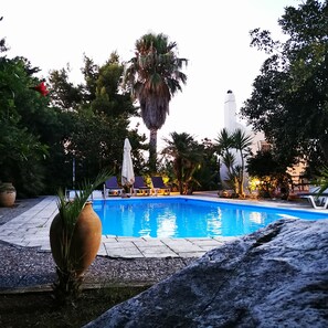 A swimming pool surrounded by palm trees and lounge chairs, with a stone pathway leading to the pool. - Villa Irene (Kos)