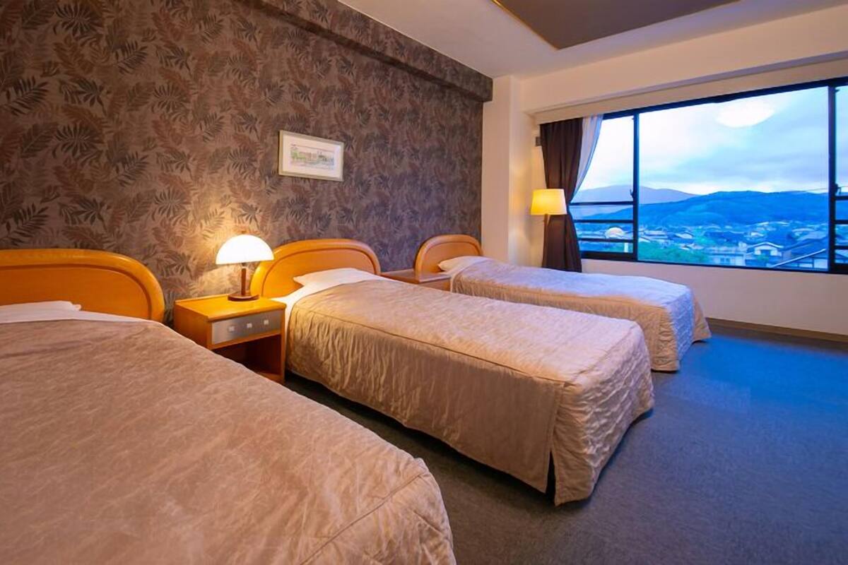 A hotel room with three beds, a large window with a view, and a patterned wall.