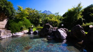 A clear pool surrounded by rocks and greenery with a mountain in the background. - Yufuin Sansuikan (Yufu)