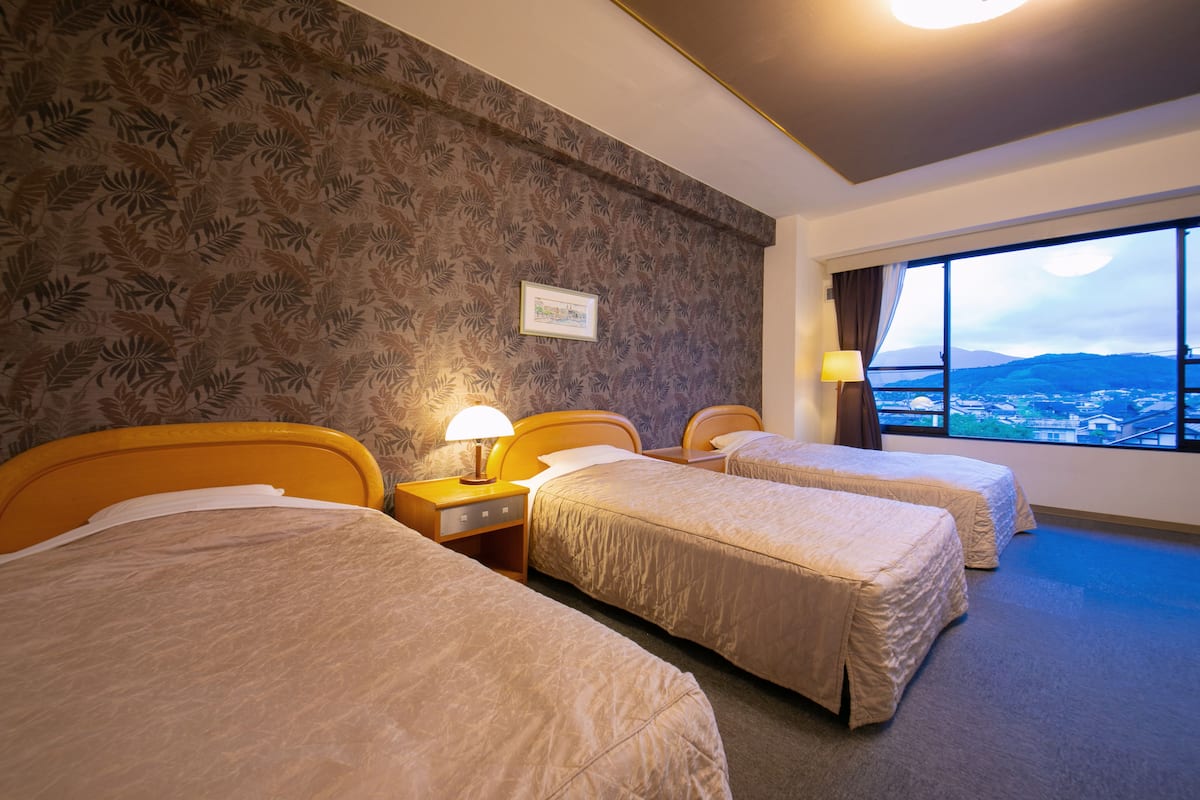 A hotel room with three beds, a large window with a view, and a patterned wallpaper.