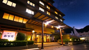 A multi-story hotel with a covered entrance, outdoor seating area, and a signboard. - Yufuin Sansuikan (Yufu)