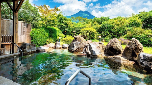 A traditional Japanese onsen with a wooden bathhouse, clear hot spring water, and a mountain in the background. - Yufuin Sansuikan (Yufu)