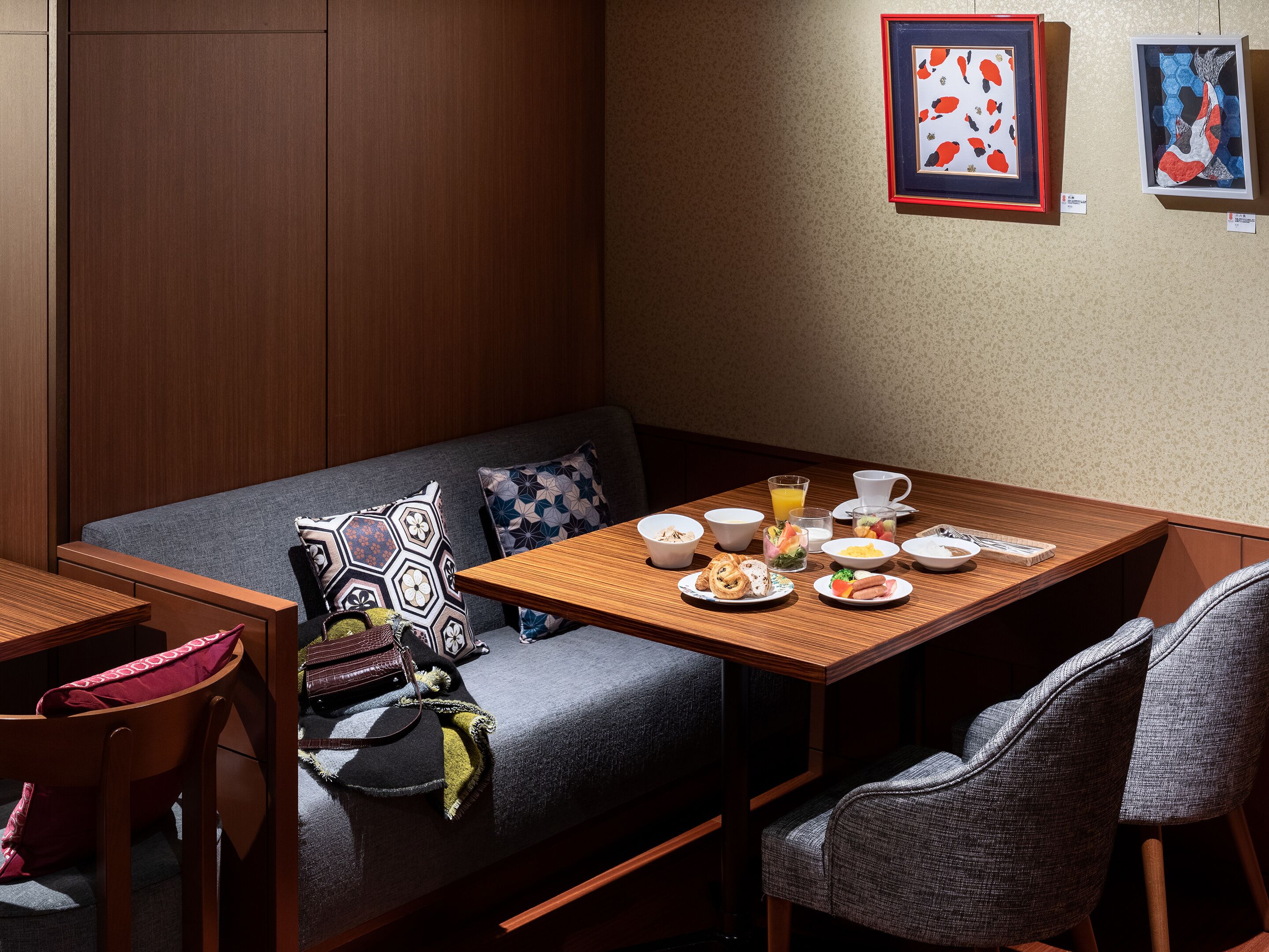 Une pièce chaleureuse avec un canapé, une table en bois dressée pour le petit-déjeuner et deux œuvres d’art encadrées accrochées au mur.