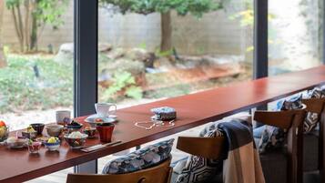 A dining area with a long table, various dishes, and a view of a garden through large windows.