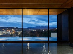 Un interior moderno con amplios ventanales que ofrecen vistas a una ciudad y montañas al atardecer.