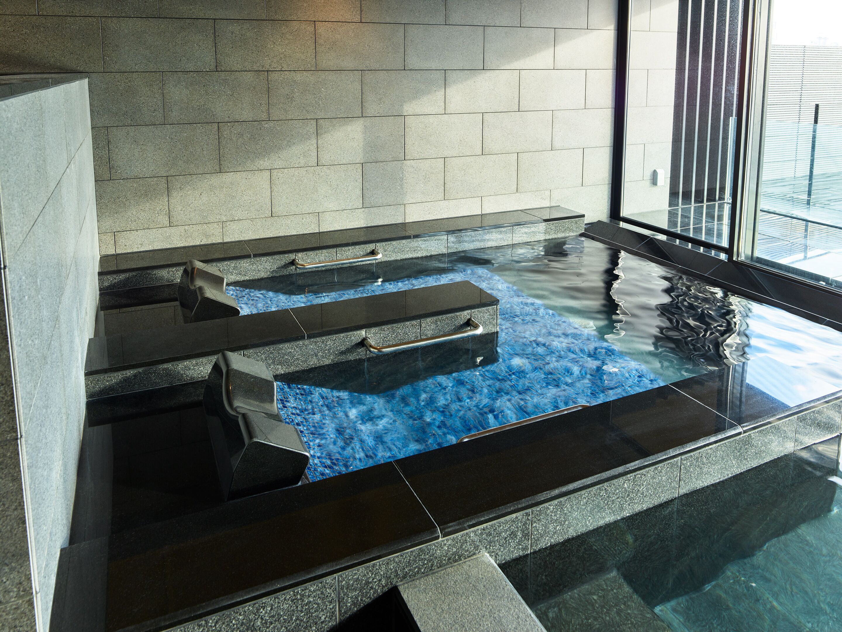 A modern indoor pool with clear water, stone steps, and a glass barrier.