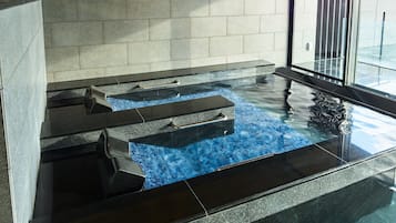A modern indoor pool with clear water, stone steps, and a glass barrier.