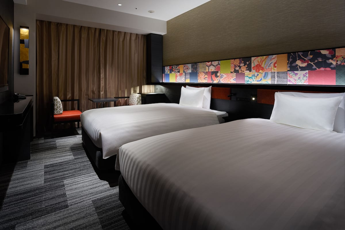 A hotel room with two beds, a desk, a chair, and a large colorful mural on the wall.