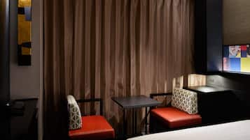 A hotel room with a bed, two red upholstered chairs, a small table, a TV, and a curtain.