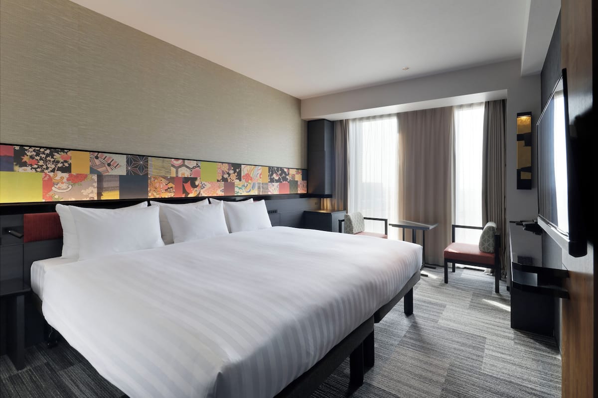 A hotel room with a large bed, a desk, a chair, a TV, and a window with curtains.