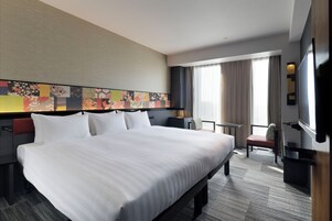 Habitación de hotel con una cama grande, un escritorio, una silla, un televisor y una ventana con cortinas.