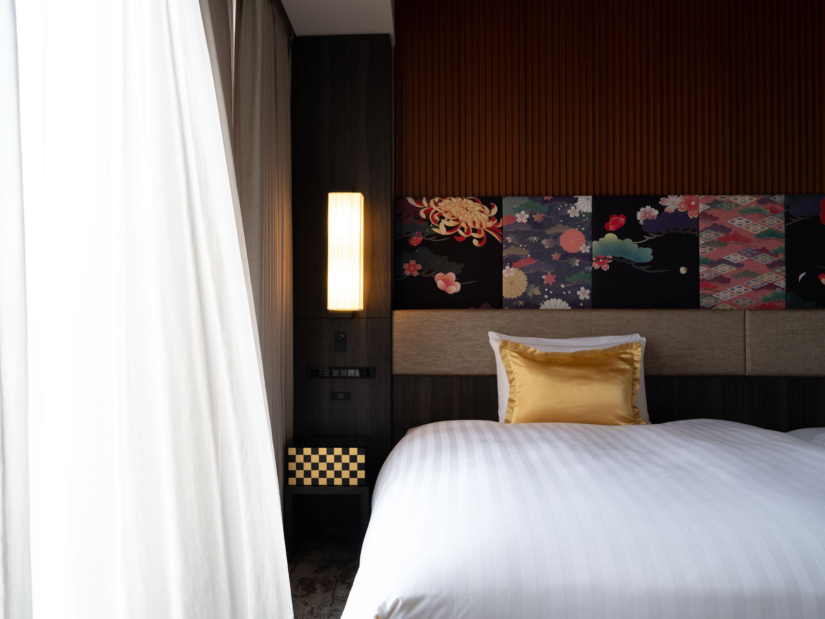 A hotel room with a bed, a nightstand, a wall-mounted lamp, and a checkered pattern on the nightstand.