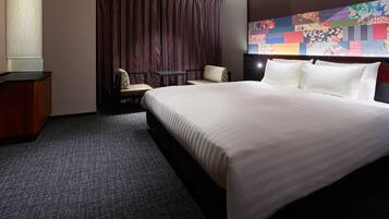 Habitación de hotel con una cama grande, un escritorio, una silla y una obra de arte colorida en la pared.