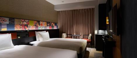 A hotel room with two beds, a desk, a chair, a TV, and a colorful wall art above the beds.