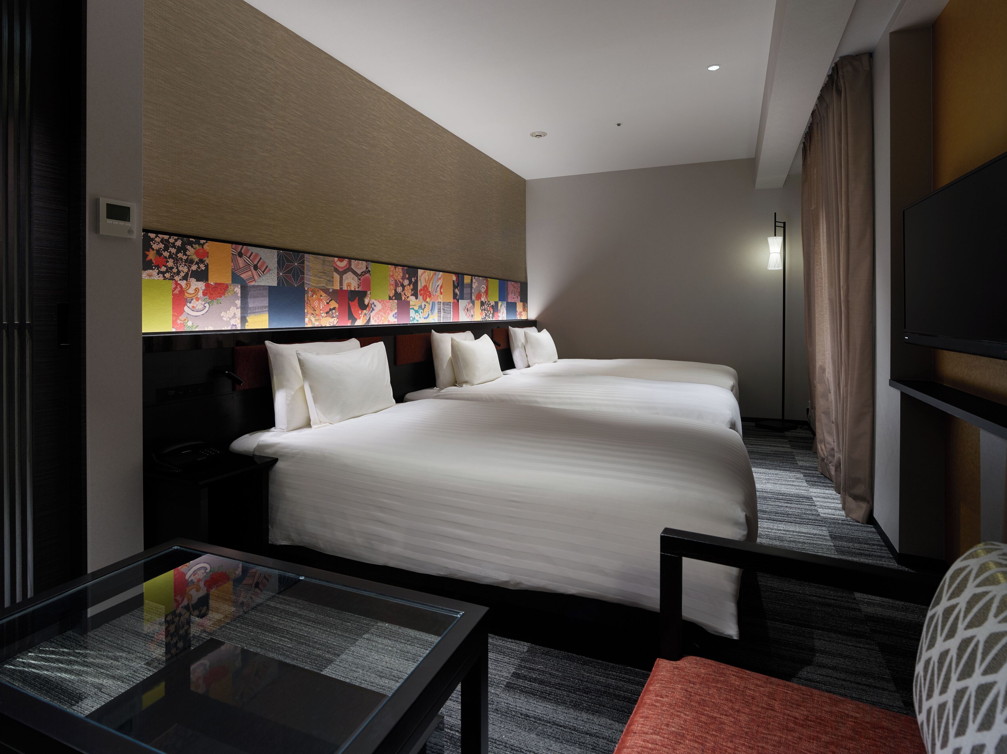 A hotel room with two beds, a flat-screen TV, a glass table with a menu, and a colorful artwork on the wall.