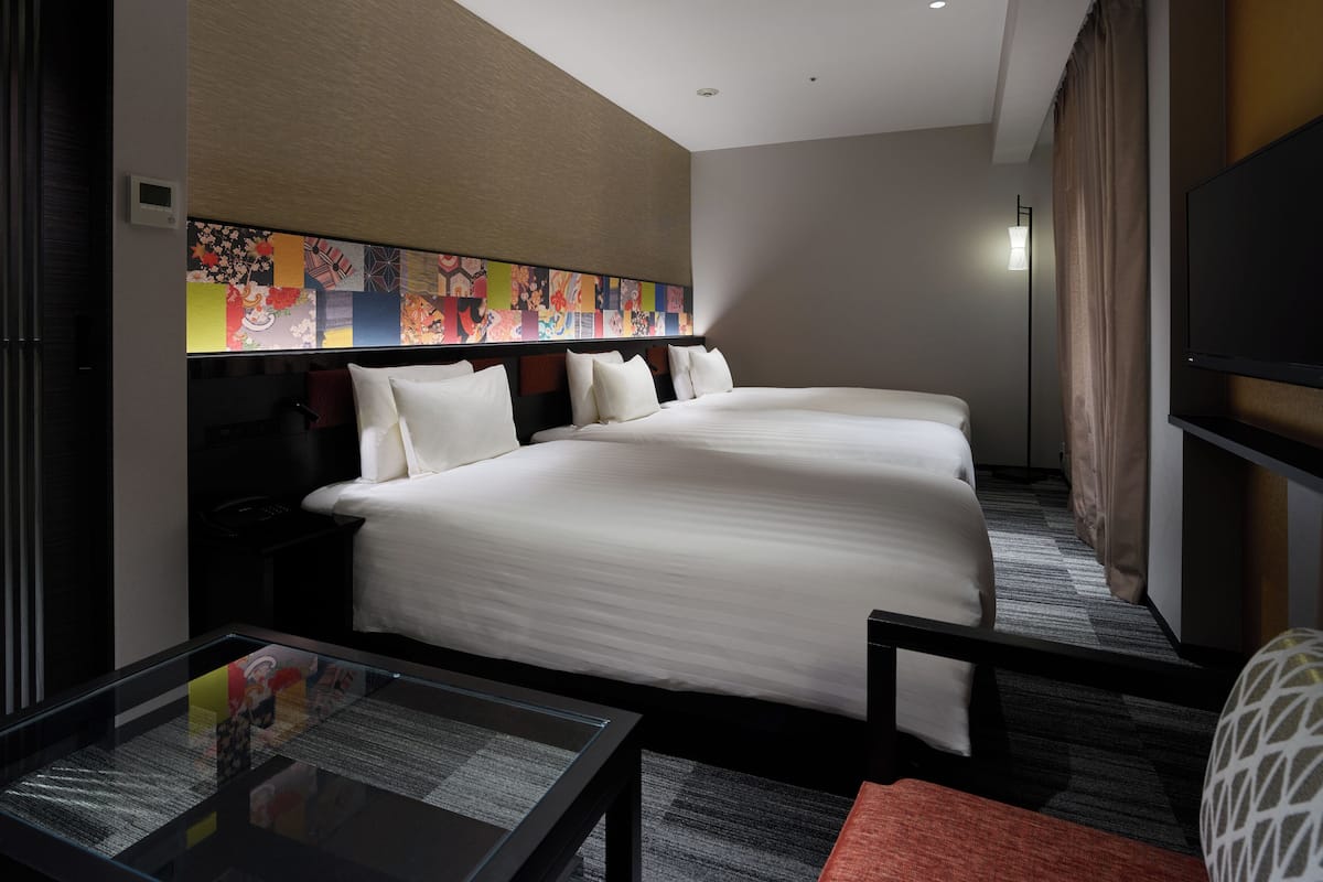 A hotel room with two beds, a flat-screen TV, a glass table with a menu, and a colorful artwork on the wall.