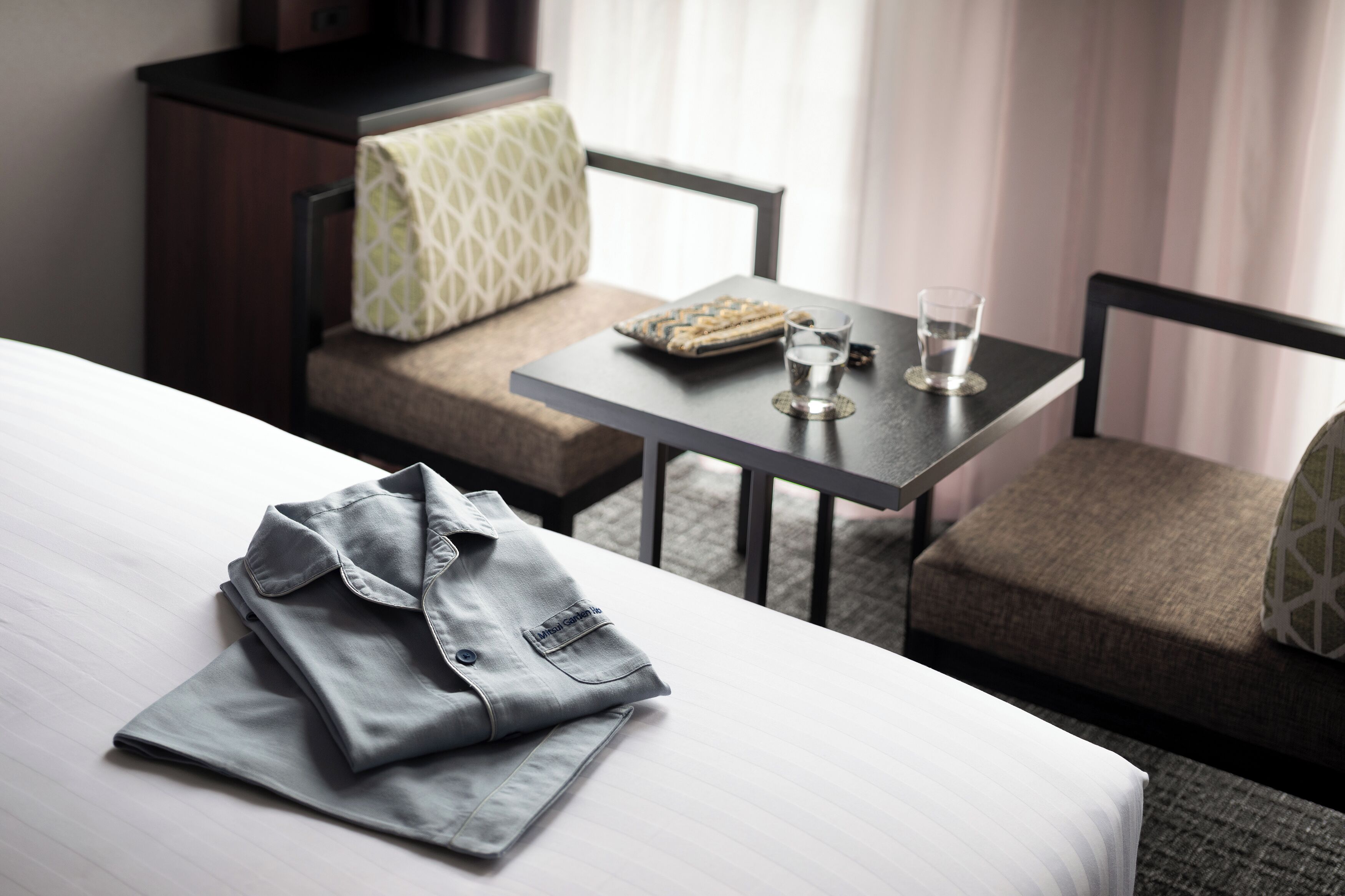 A neatly made bed with a folded shirt and a small tray on a table beside a sofa.