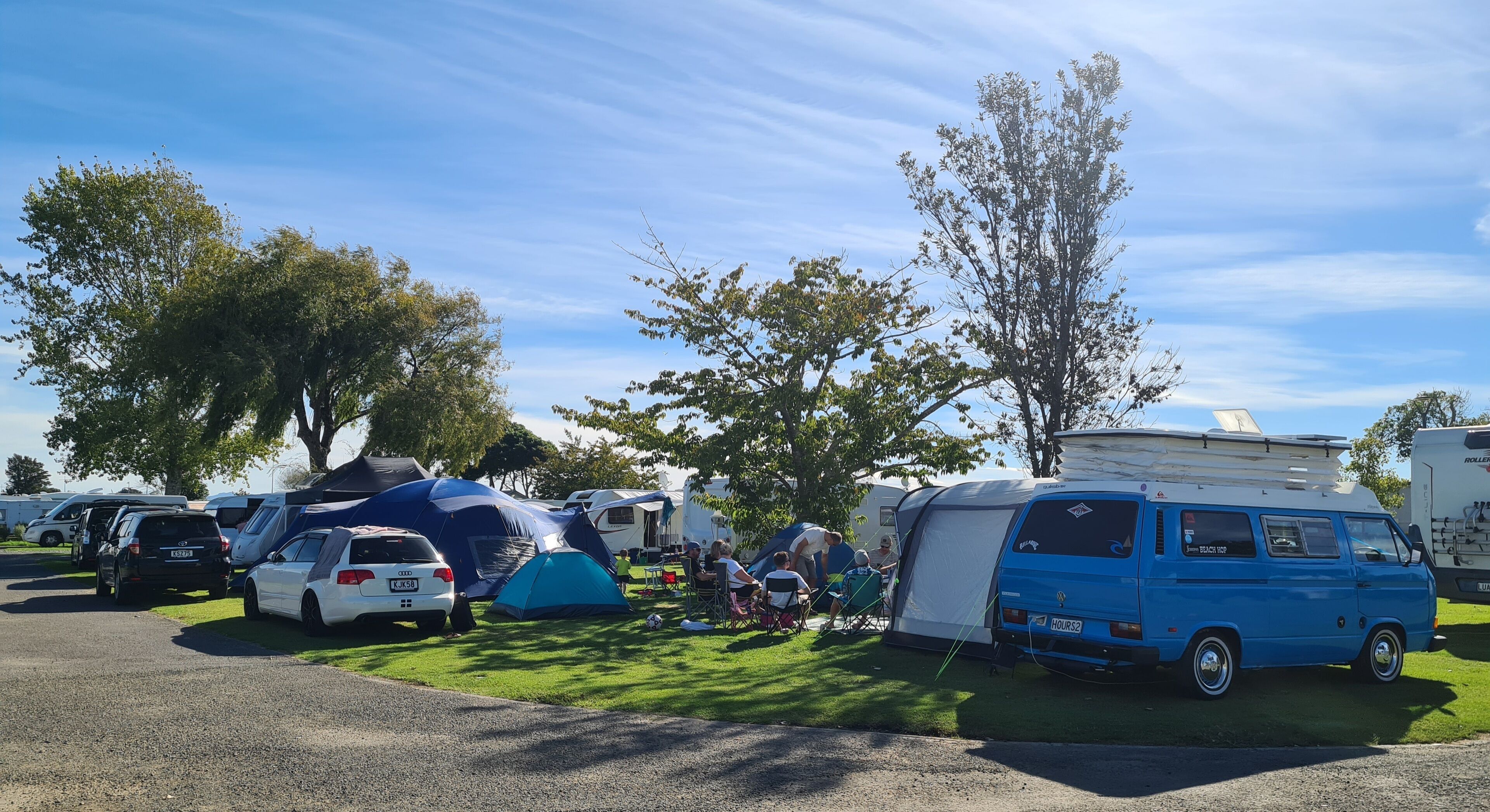 Un camping con vehículos recreativos y tiendas de campaña, zonas de césped y árboles.