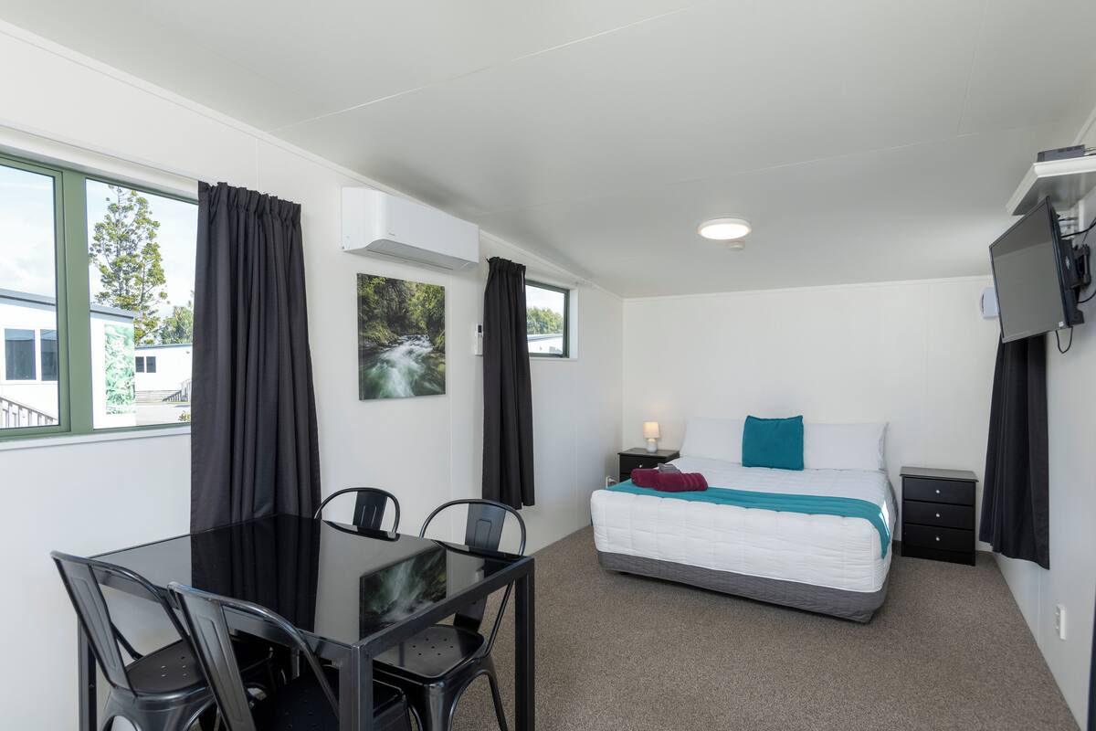 Een hotelkamer met een bed, een bureau met stoelen, een televisie en een raam met gordijnen.