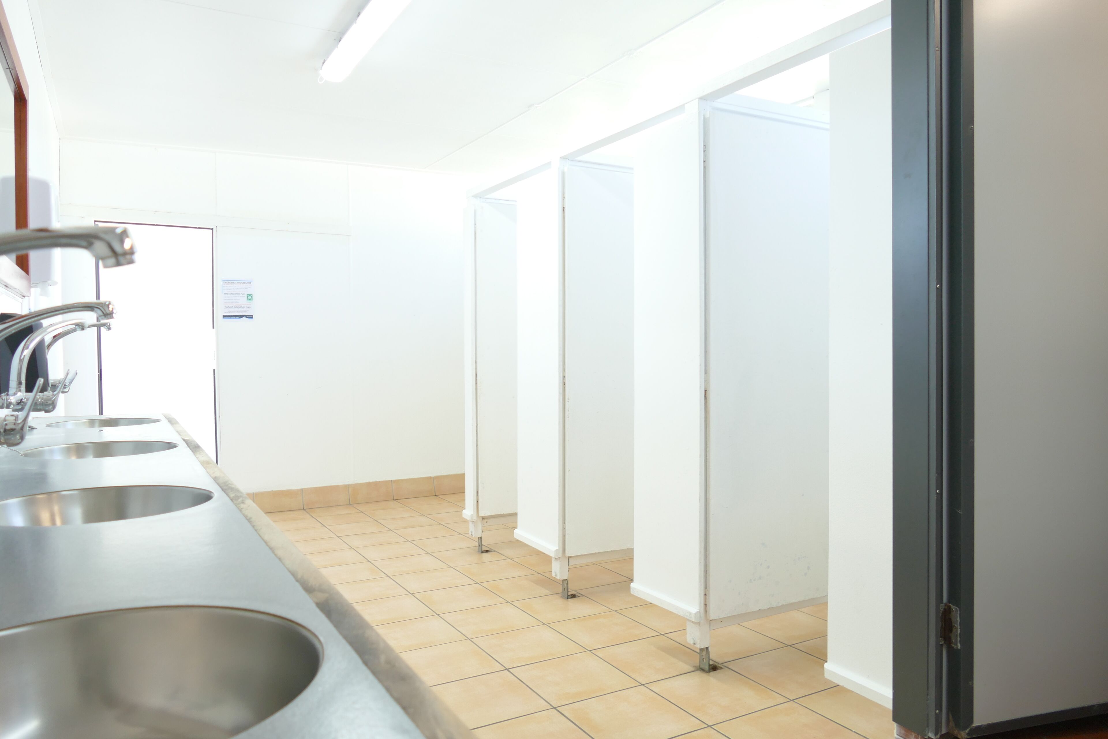 Baño público con tres lavamanos, un espejo y una puerta que da a otra habitación.