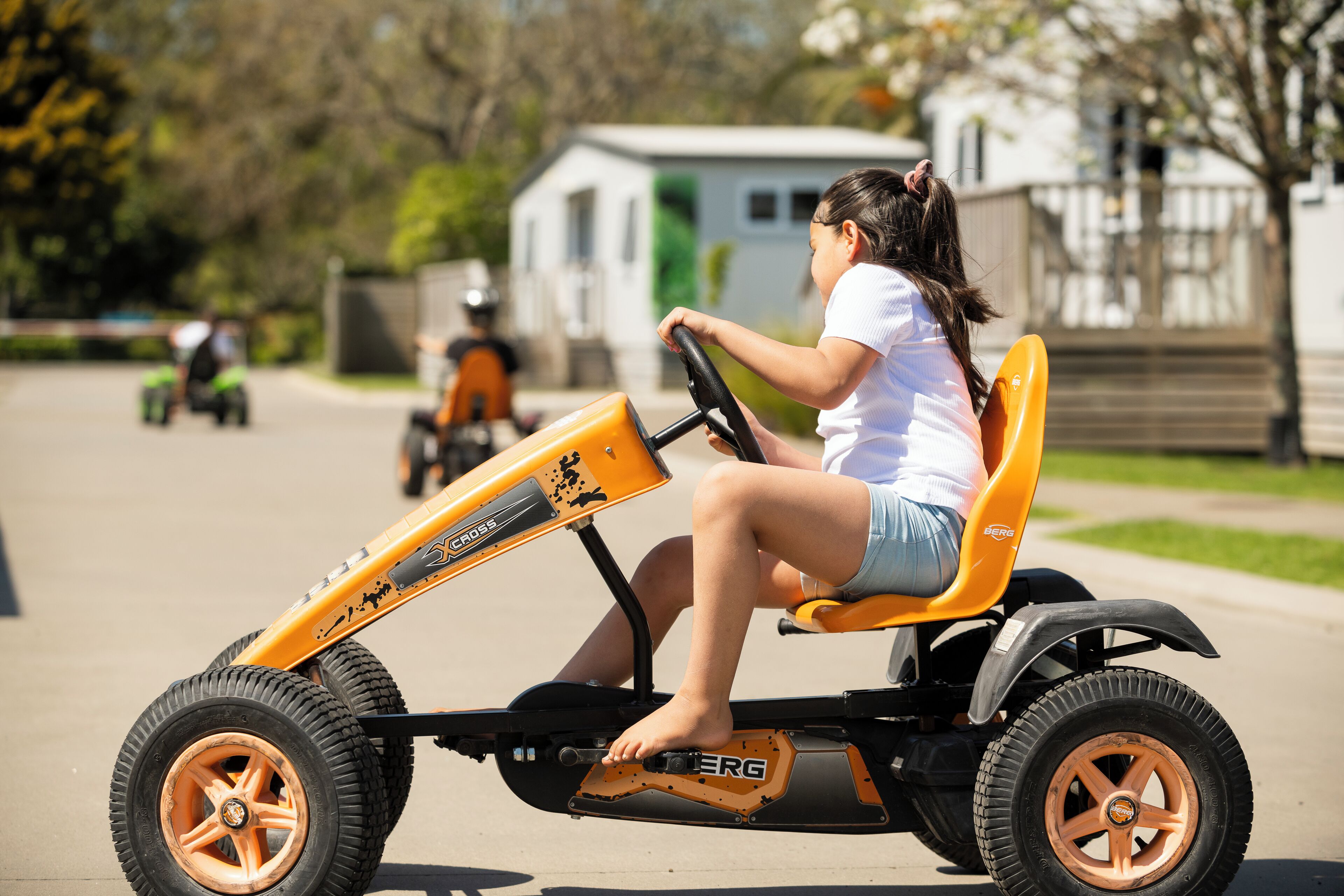 A child driving a small, orange go-kart on a residential street.
