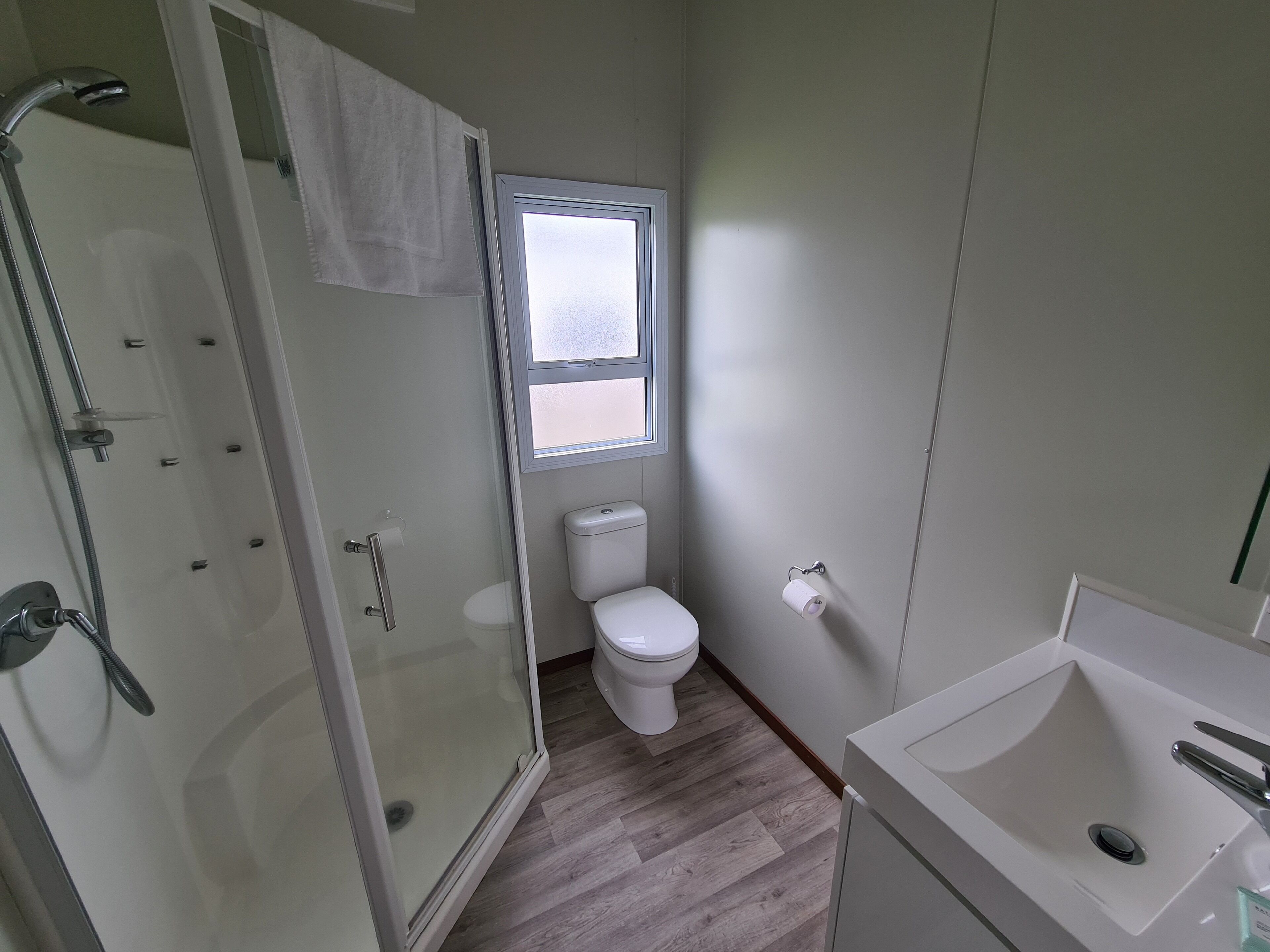 A compact bathroom with a glass-enclosed shower, a toilet, and a sink.