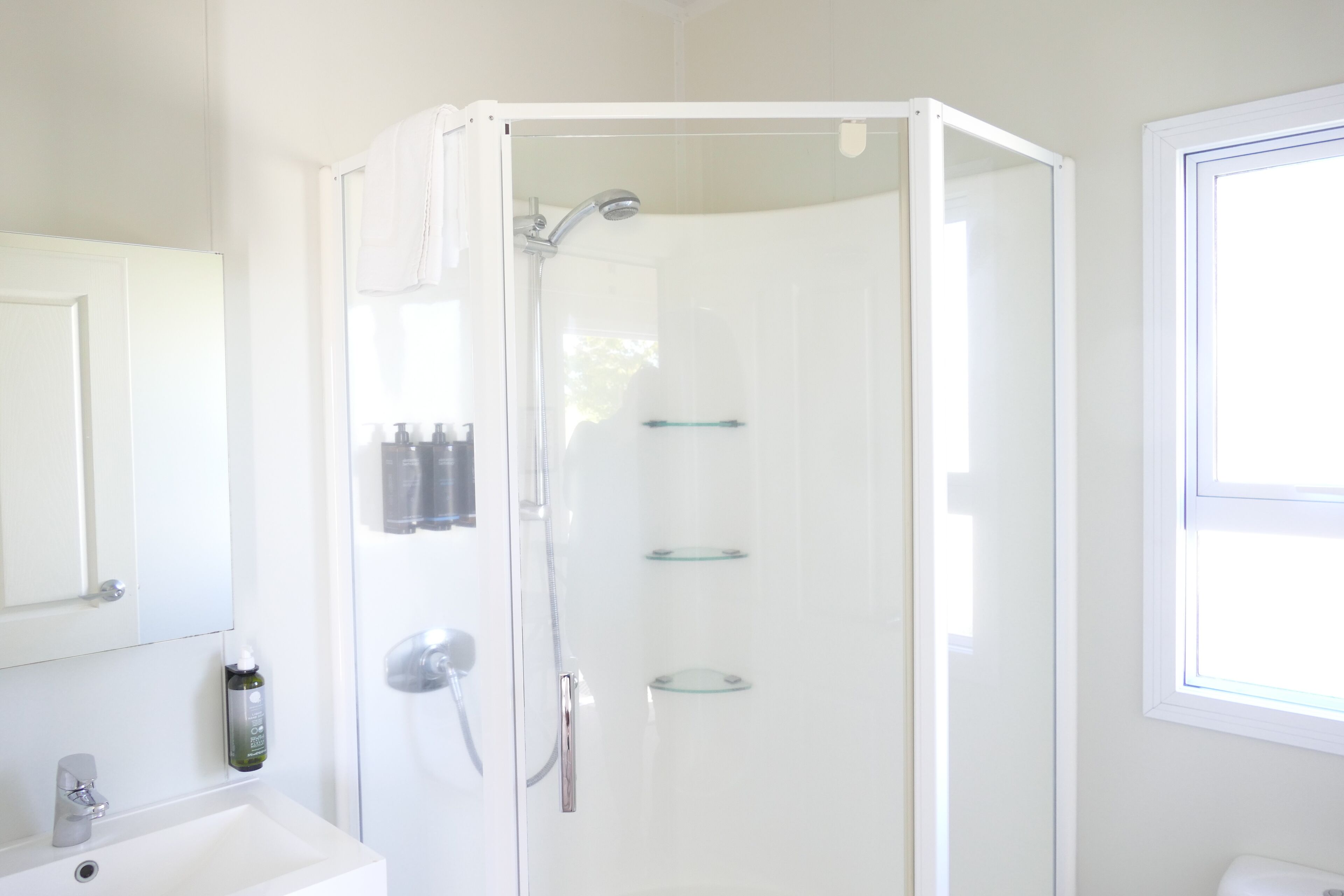 A modern bathroom with a glass-enclosed shower, a white sink, and a large mirror.