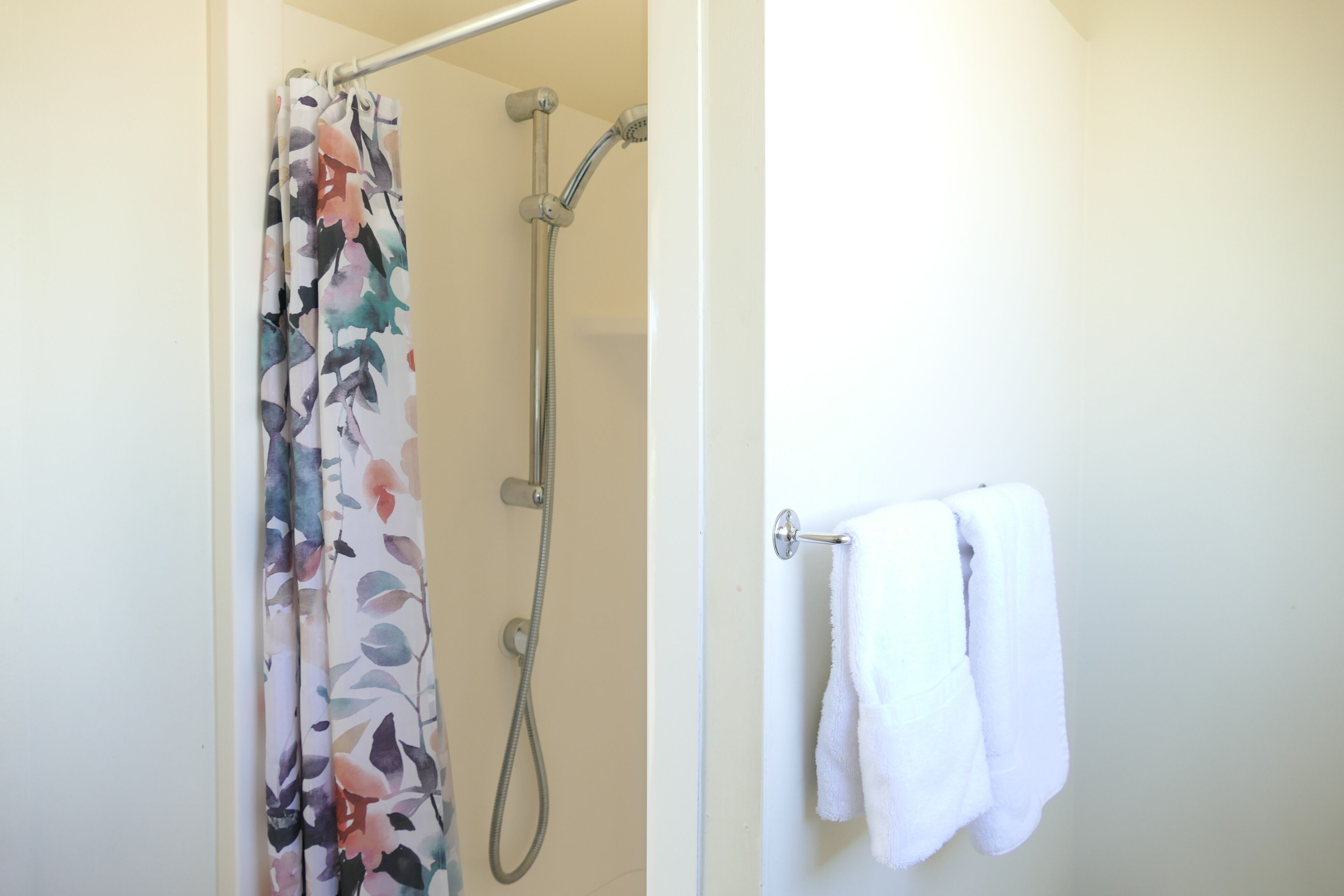 Un baño con cortina de ducha, un perchero con dos toallas y un cabezal de ducha.