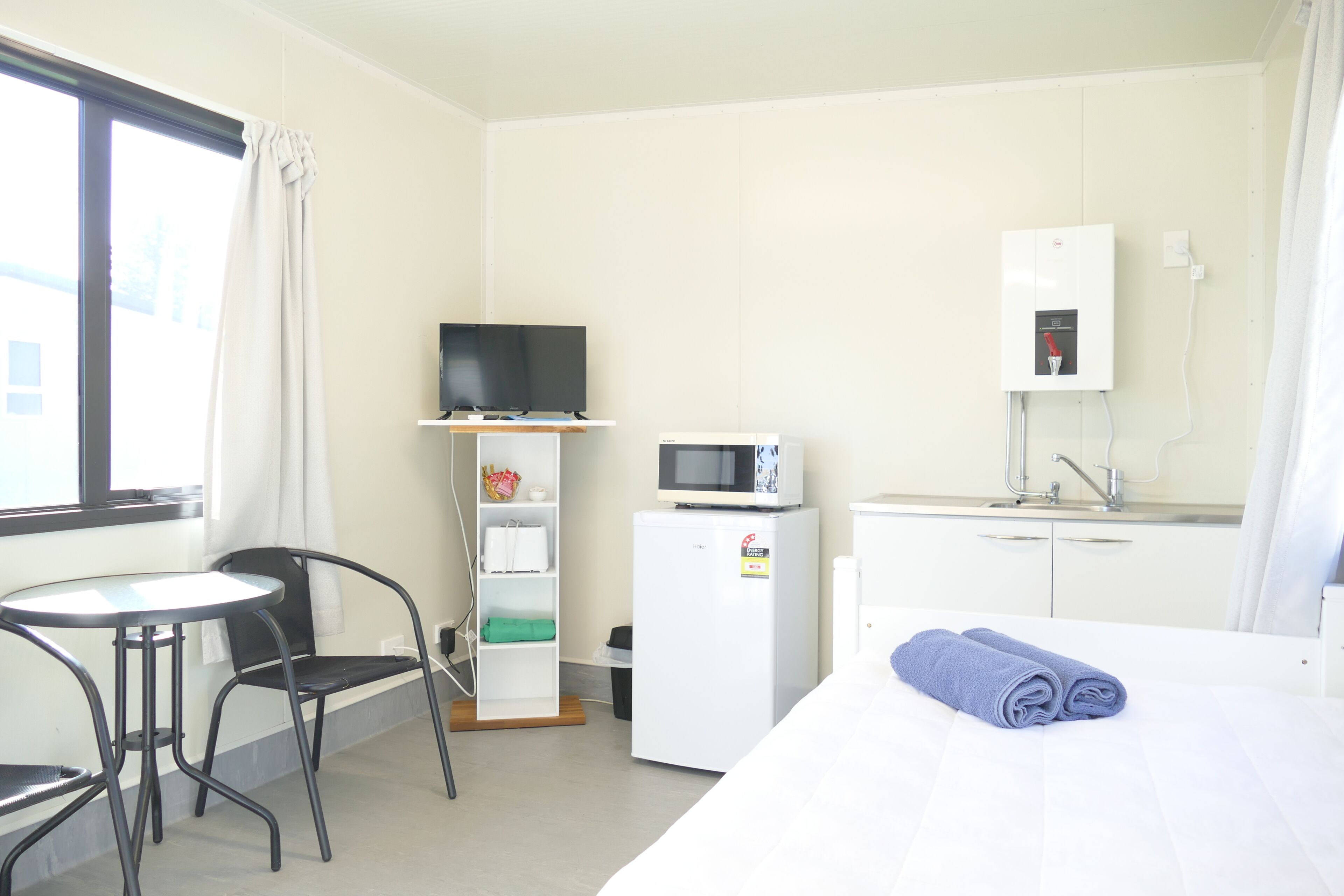 A hotel room with a bed, a small desk, a chair, a television, a microwave, a refrigerator, and a window with curtains.