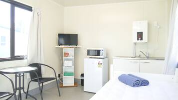 A hotel room with a bed, a small desk, a chair, a television, a microwave, a refrigerator, and a window with curtains.