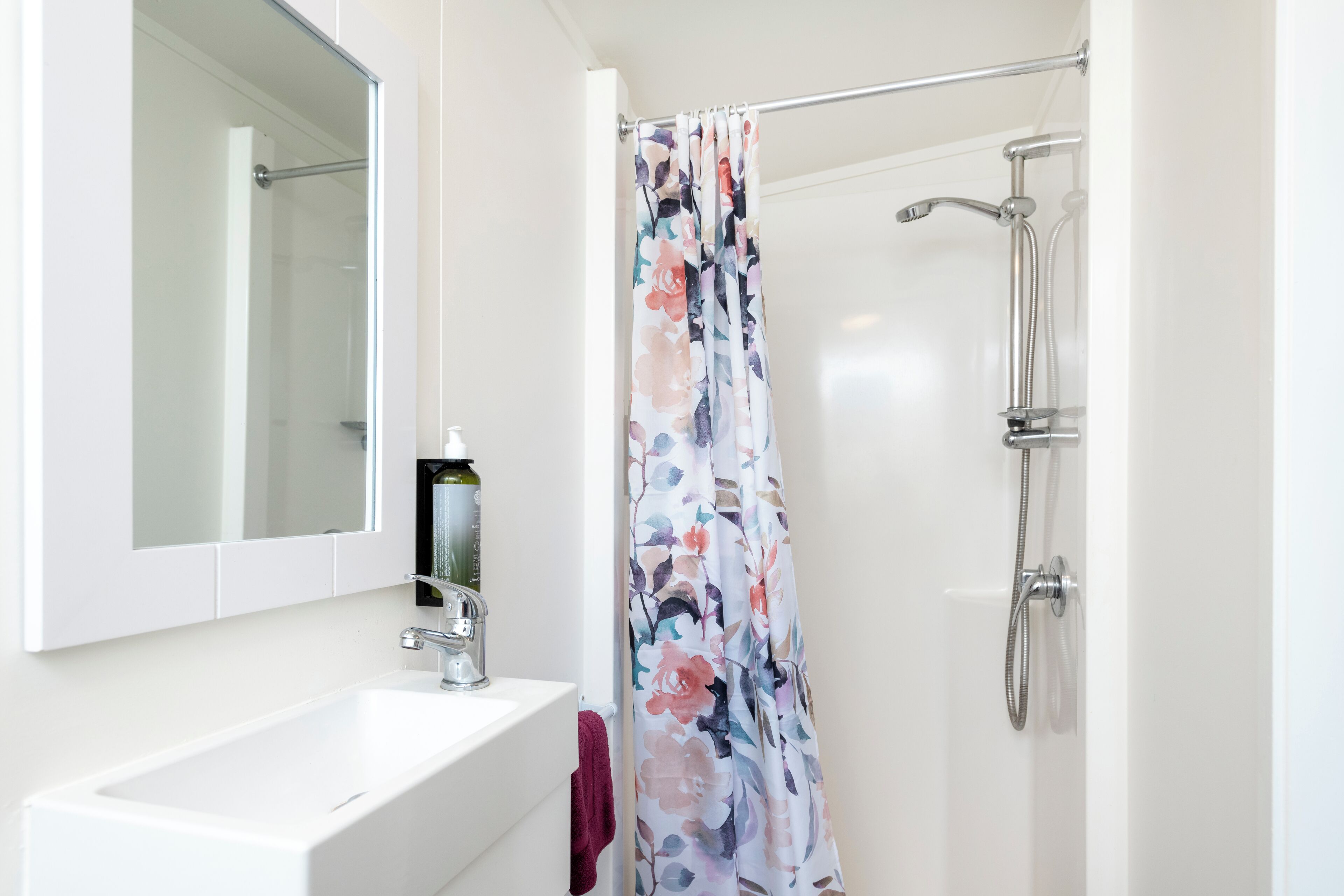 A bathroom with a white sink, a mirror, a shower with a floral shower curtain, and a handheld showerhead.
