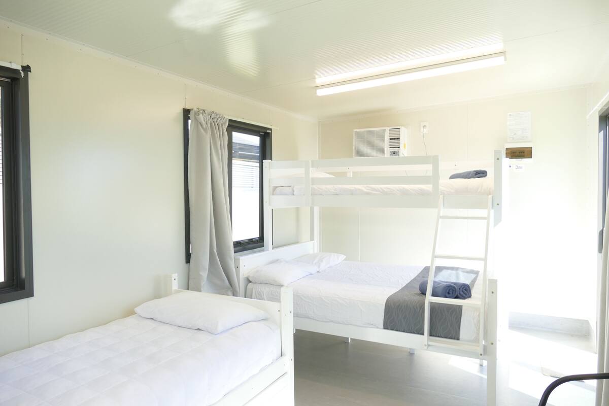 Een slaapkamer met stapelbed, raam, gordijnen en een wandairconditioner.