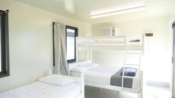 Een slaapkamer met stapelbed, raam, gordijnen en een wandairconditioner.