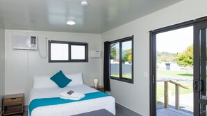 A hotel room with a bed, a bench, a window, an air conditioning unit, and a door leading to a balcony.