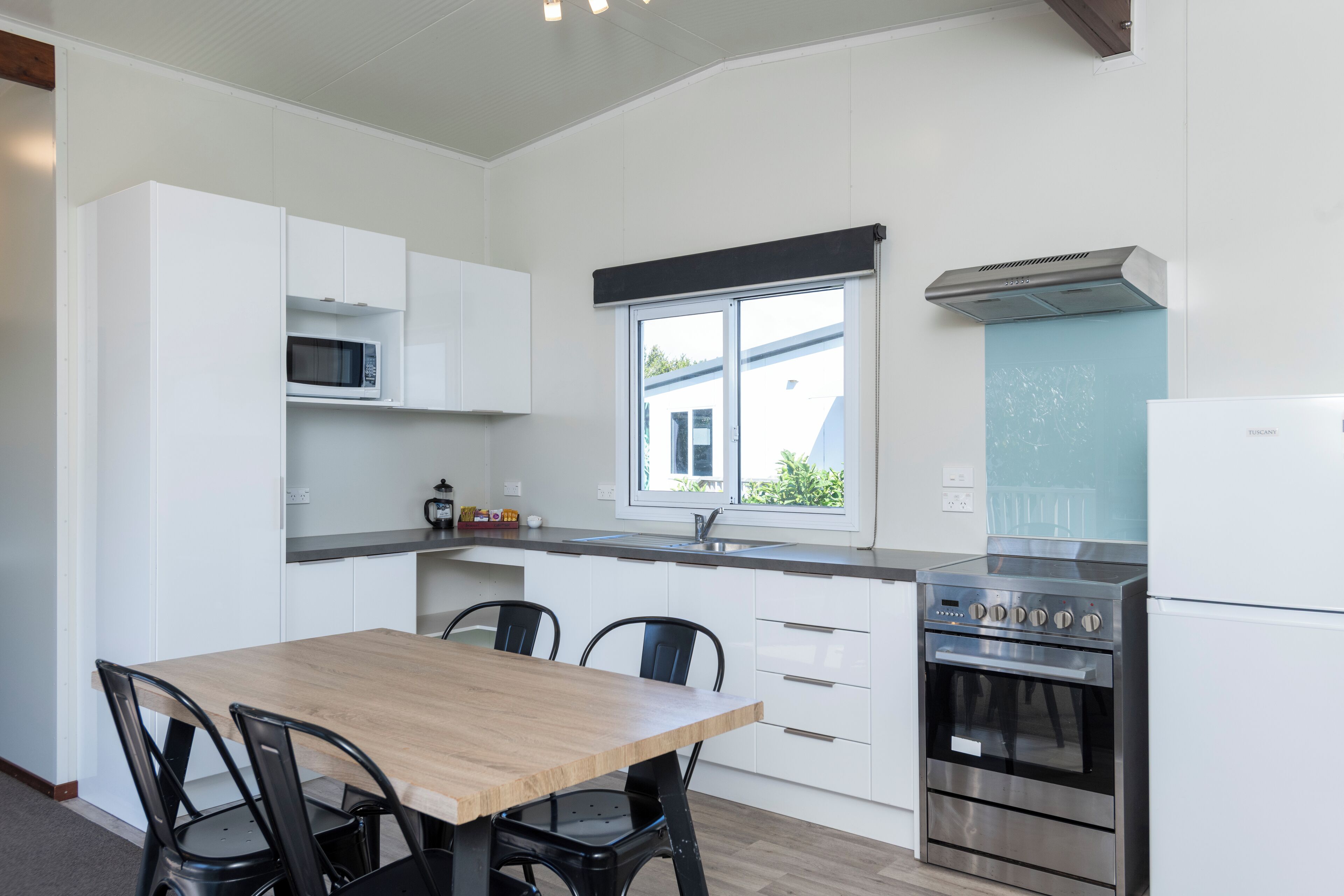 A modern kitchen with white cabinets, a wooden dining table, and black chairs.