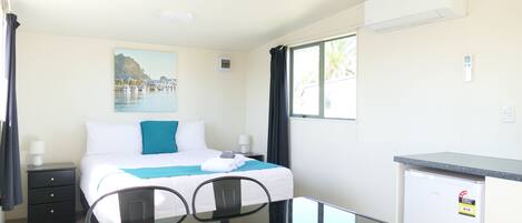 Habitación de hotel con cama, escritorio, silla, refrigerador pequeño y ventana con cortinas.