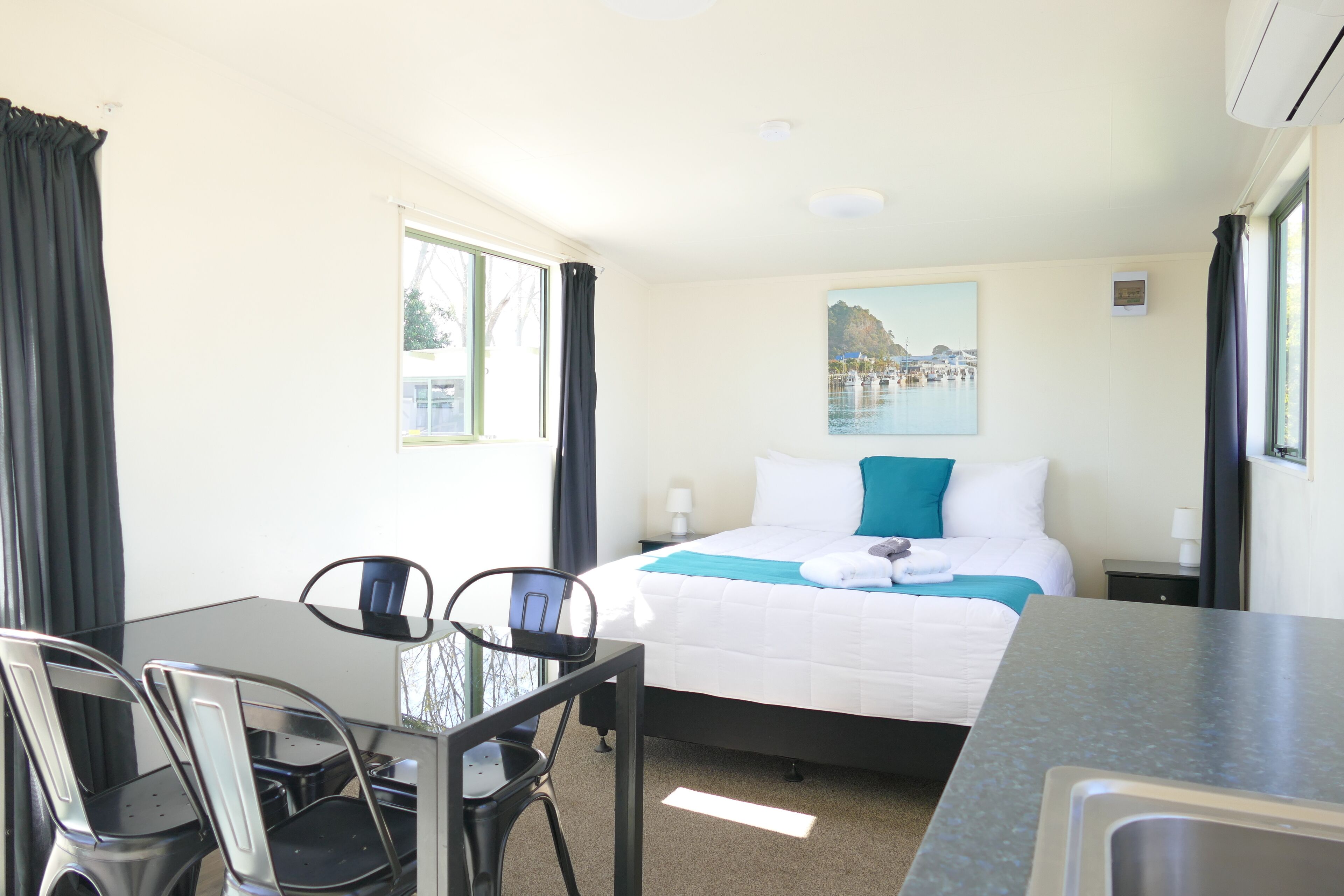 Een hotelkamer met een bed, een bureau met stoelen, een raam met gordijnen en een schilderij aan de muur.
