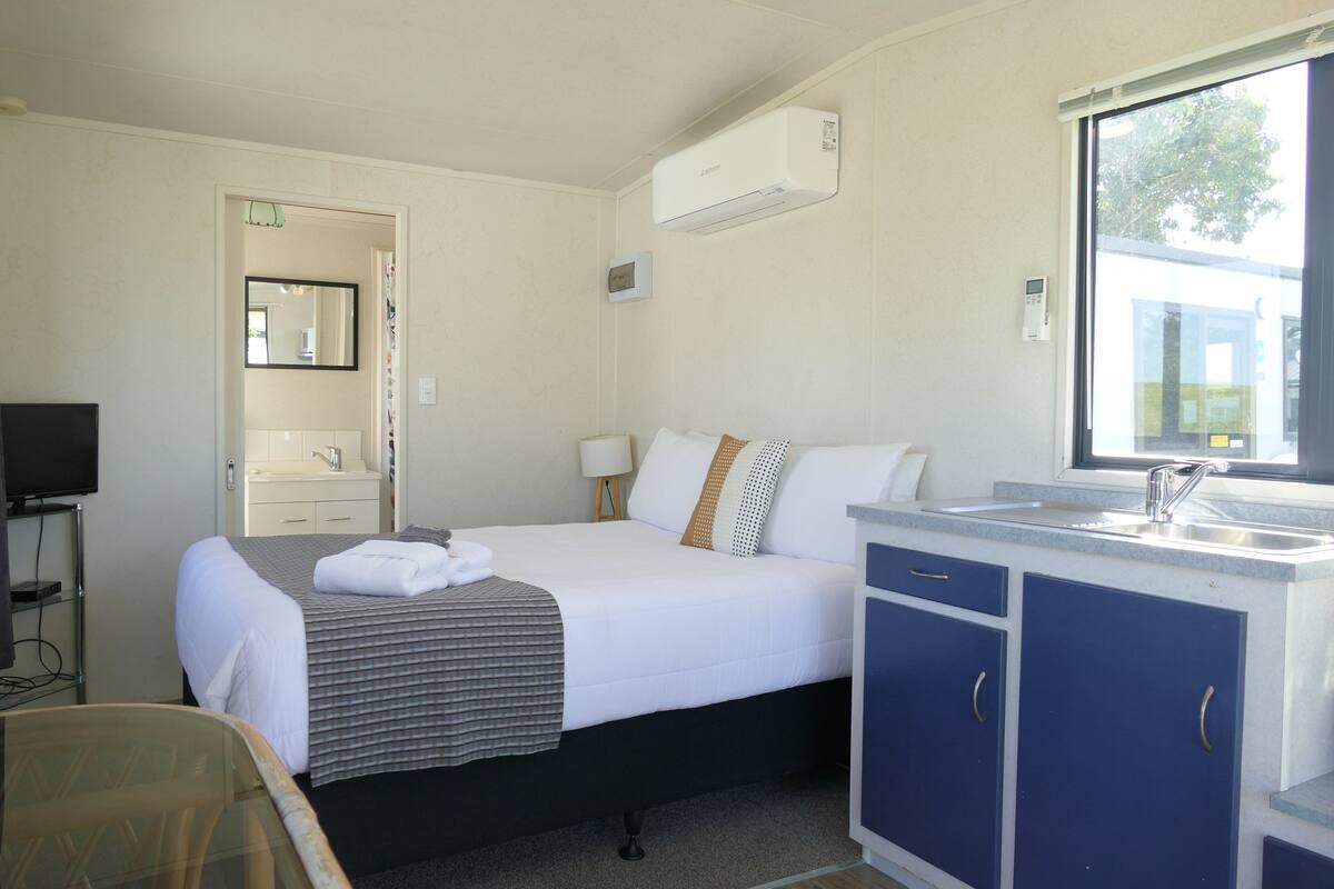 Een hotelkamer met een bed, nachtkastje, televisie, raam en een badkamer die door een geopende deur zichtbaar is.