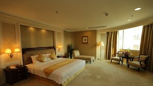 Habitación de hotel con una cama grande, lámparas de noche, una mesita con sillas y un ventanal con cortinas.
