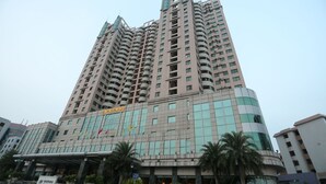Un hotel de varios pisos con diseño moderno, que destaca por su entrada con un paseo cubierto y palmeras.